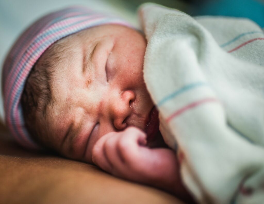 Through the lens of birth photography right after birth this baby is resting on his mother's chest with his eyes closed and looking beautiful and pink. Photographed by Dear Birth in west Los Angeles.