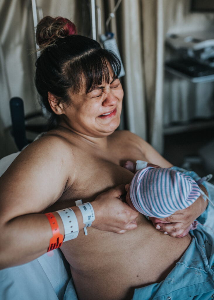 Image of crying woman as she latches her baby to her chest for the first time. This image was portrayed in the Interview with KCRW with Los Angeles birth photographer & Videographer Diana Hinek for Dear Birth