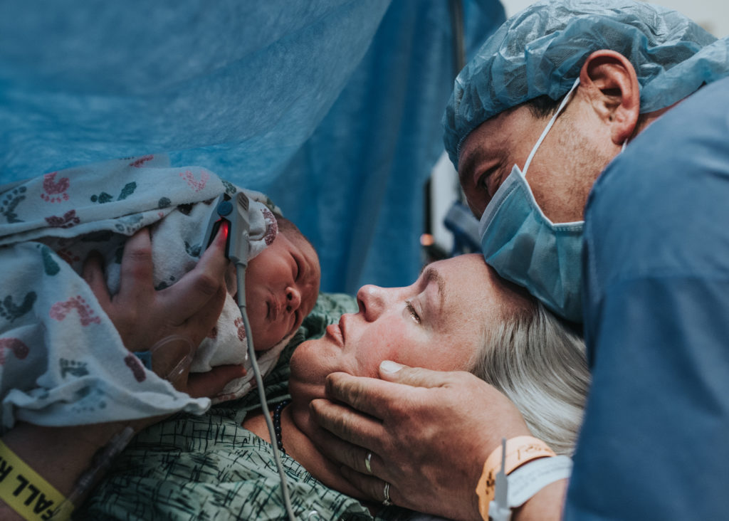 Color image of mother and father meeting their baby girl right after a cesarean birth. Image by Los Angeles birth photographer Diana Hinek for #dearbirth during Cesarean awareness month