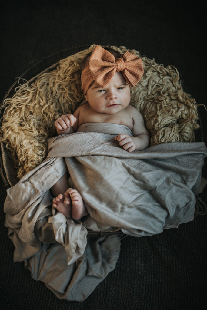 Color image of newborn baby in a fluffy basket wearing a bow on her head and loking at the cameraduring a fresh 48 newborn session with Los Angeles Birth Photographer Diana Hinek for ArtShaped Photography