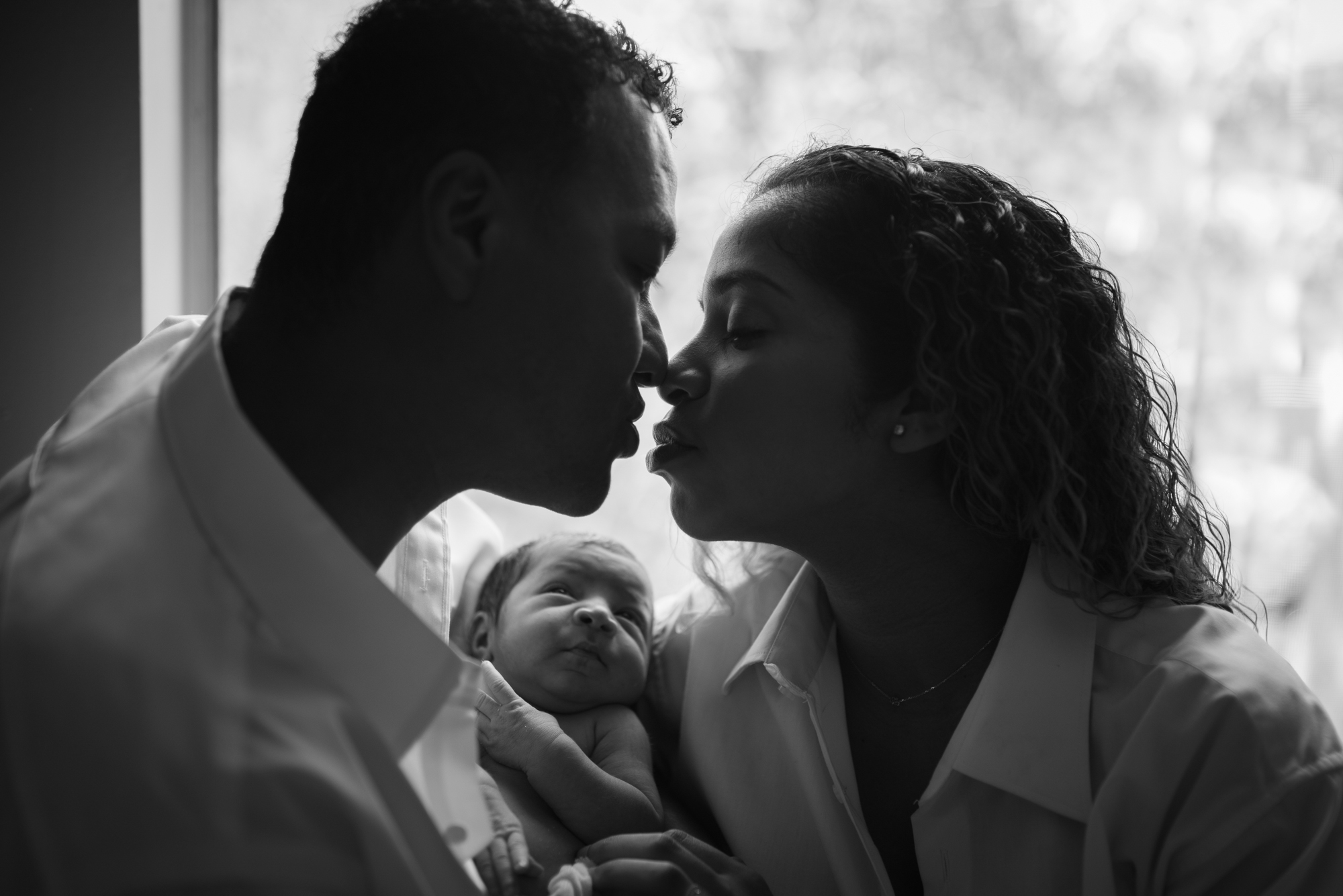 black and white image of parents kissing while baby looks up at them as photographed by Los Angeles Santa Monica family Photographer Diana Hinek