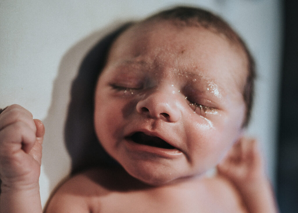 Image of when big brother meets his newborn baby brother. Color image of newborn baby with eyes closed, moments after his birth. Image courtesy of Los Angeles birth photographer Diana Hinek for #dearbirth.