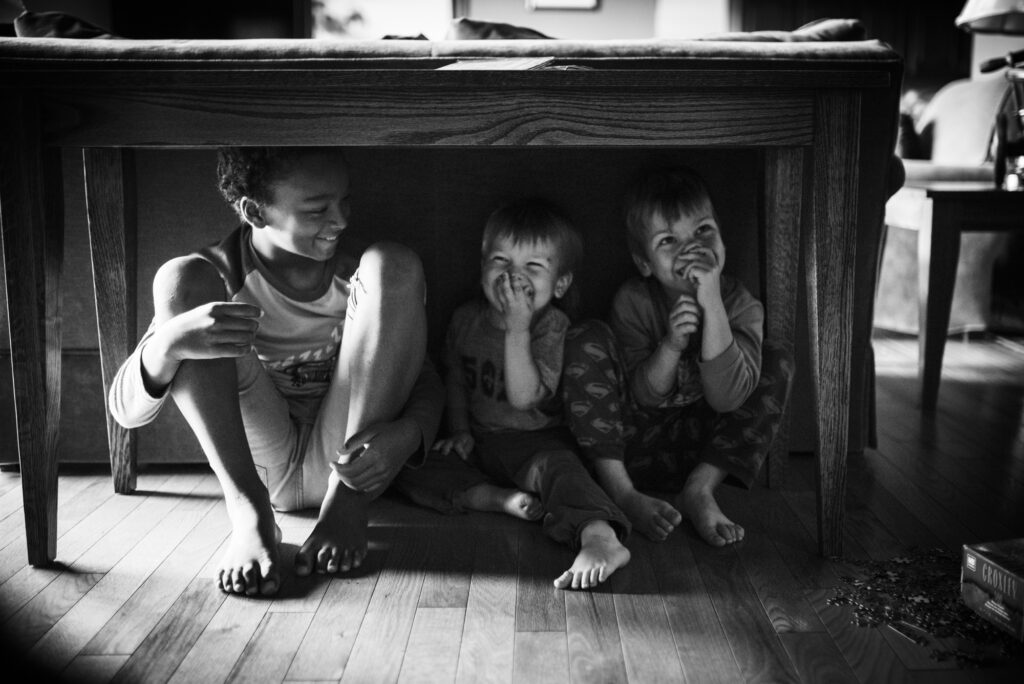Candid shot of Siblings hiding under a table at home, the perfect family photo taken by professional family photograher