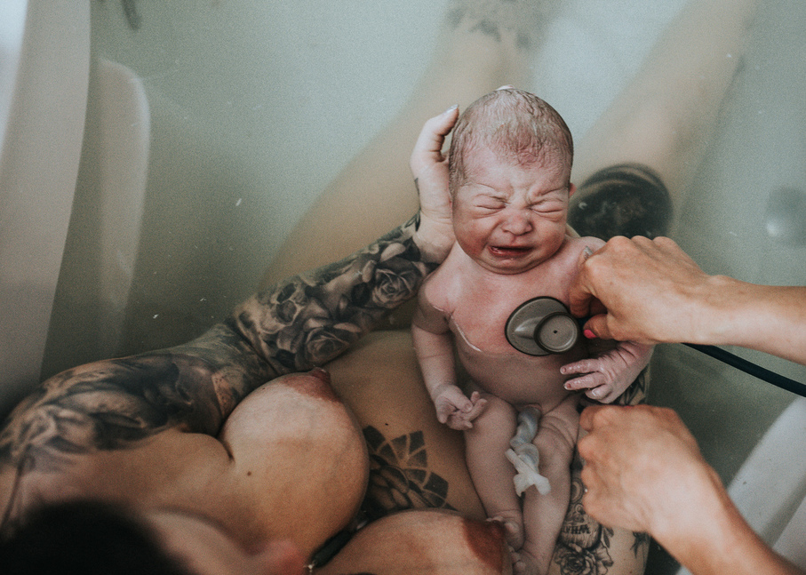 Newborn baby getting examined right after birth still in the water as captured by Los Angeles birth photographer and videographer Diana Hinek for Dear Birth