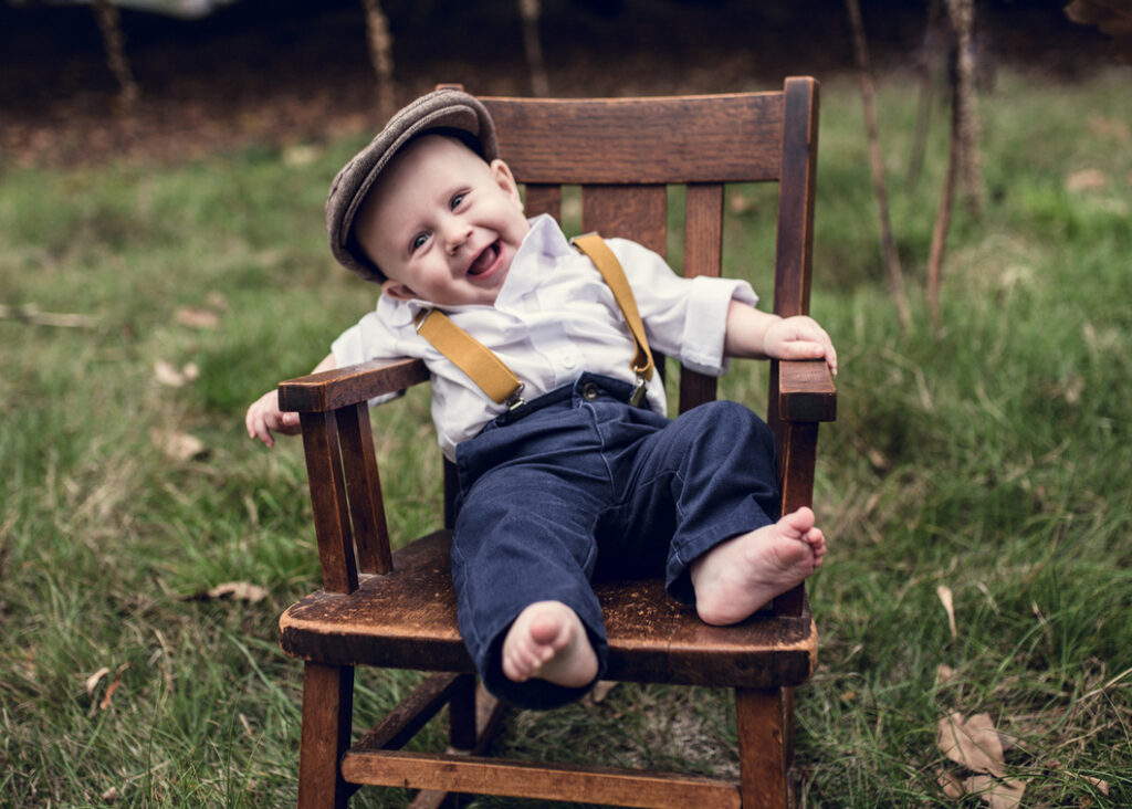 Baby poses on a rocking chair while smiling as photographed by Black and white image of Grandparents with all the grandchildren photographed by Los Angeles Family photographer Dear Birth