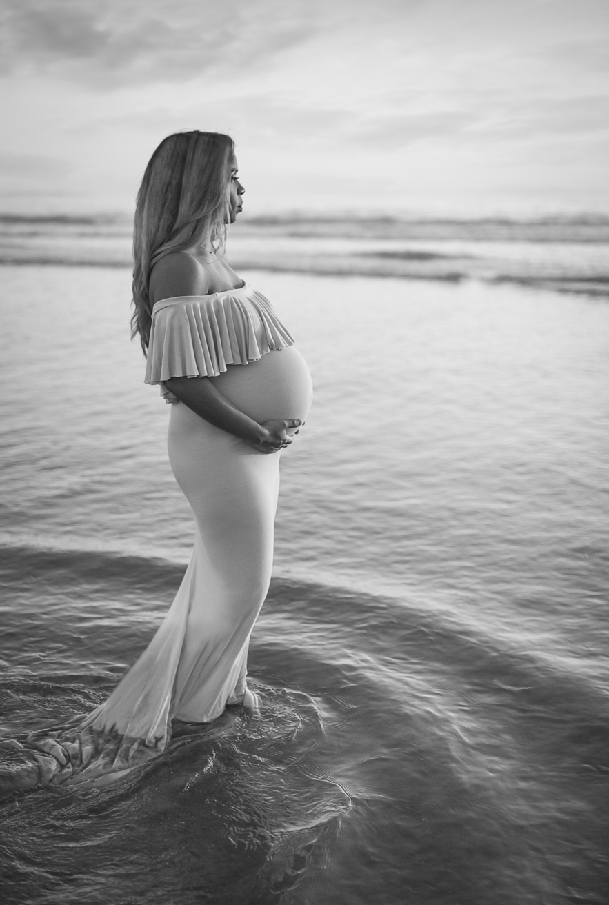 Black and white image of pregnant woman looking out to the ocean as photographed by Los Angeles prengancy and newborn photographer and videographer Diana Hinek for Dear Birth