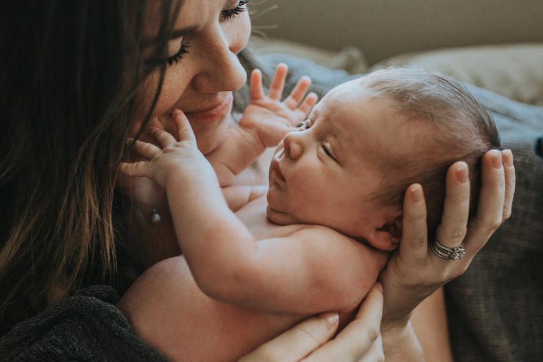 Mother looks at her newborn baby as he reaches out to touch her face as photographed by Los Angeles Pregnancy & Newborn Birth Photographer Diana Hinek for Dear Birth