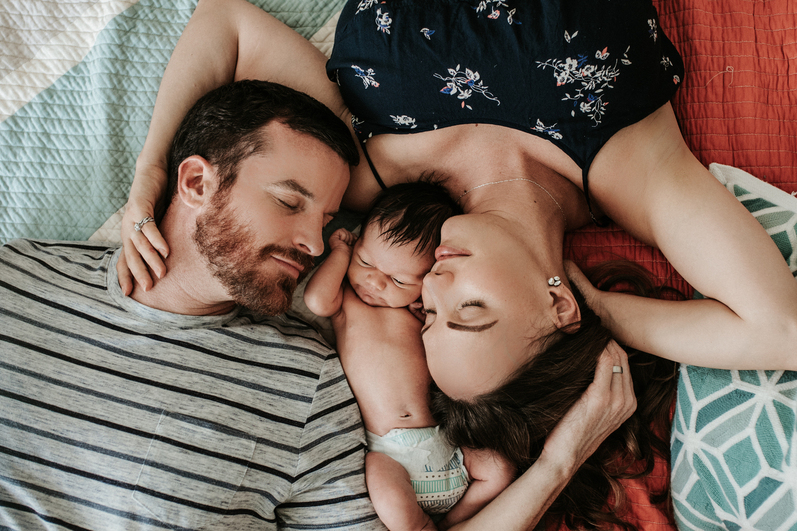 Color image of family of three top view cuddling on the bed as photographed by Los Angeles Pregnancy and newborn photographer Diana Hinek for Dear Birth