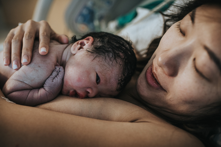 Color image of mother holding a newborn baby over her chest right after birth, captured by Los Angeles birth photographer Diana Hinek for dear birth.