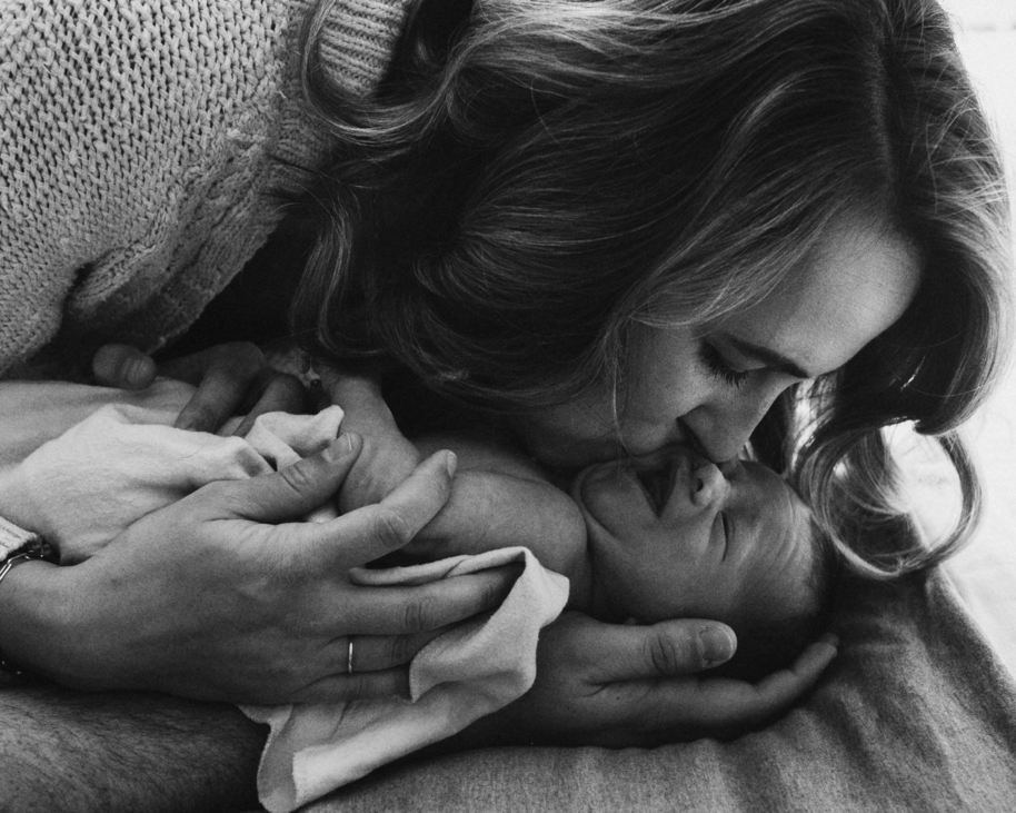 Black and white image of mom leaning down to kiss baby as captured by Los Angeles newborn photographer Diana Hinek for Dear Birth