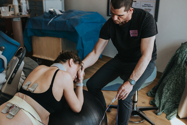 Color-image-woman-in-labor-leaning-against-birth-ball-wearing-a-tens-unit