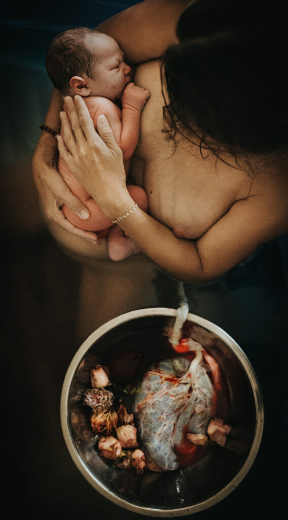 Color image of mother holding her baby right after birth. Baby is still attached to his Placenta via the umbilical cord. Image captured by Los Angeles Birth Photographer Diana Hinek for Dear Birth